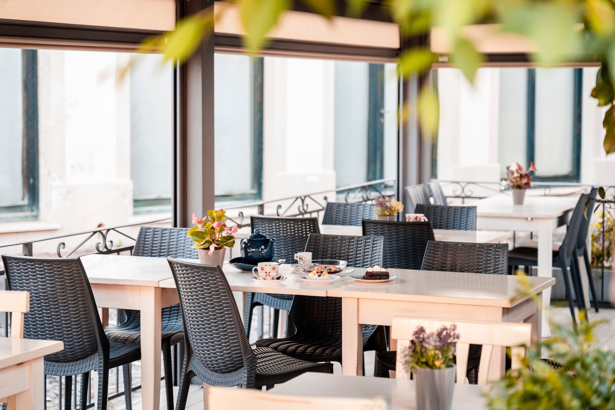 Dehors del Manu Bar Trattoria con tavoli bianchi, sedie intrecciate grigie, teiera blu, dolci e vasetti di fiori